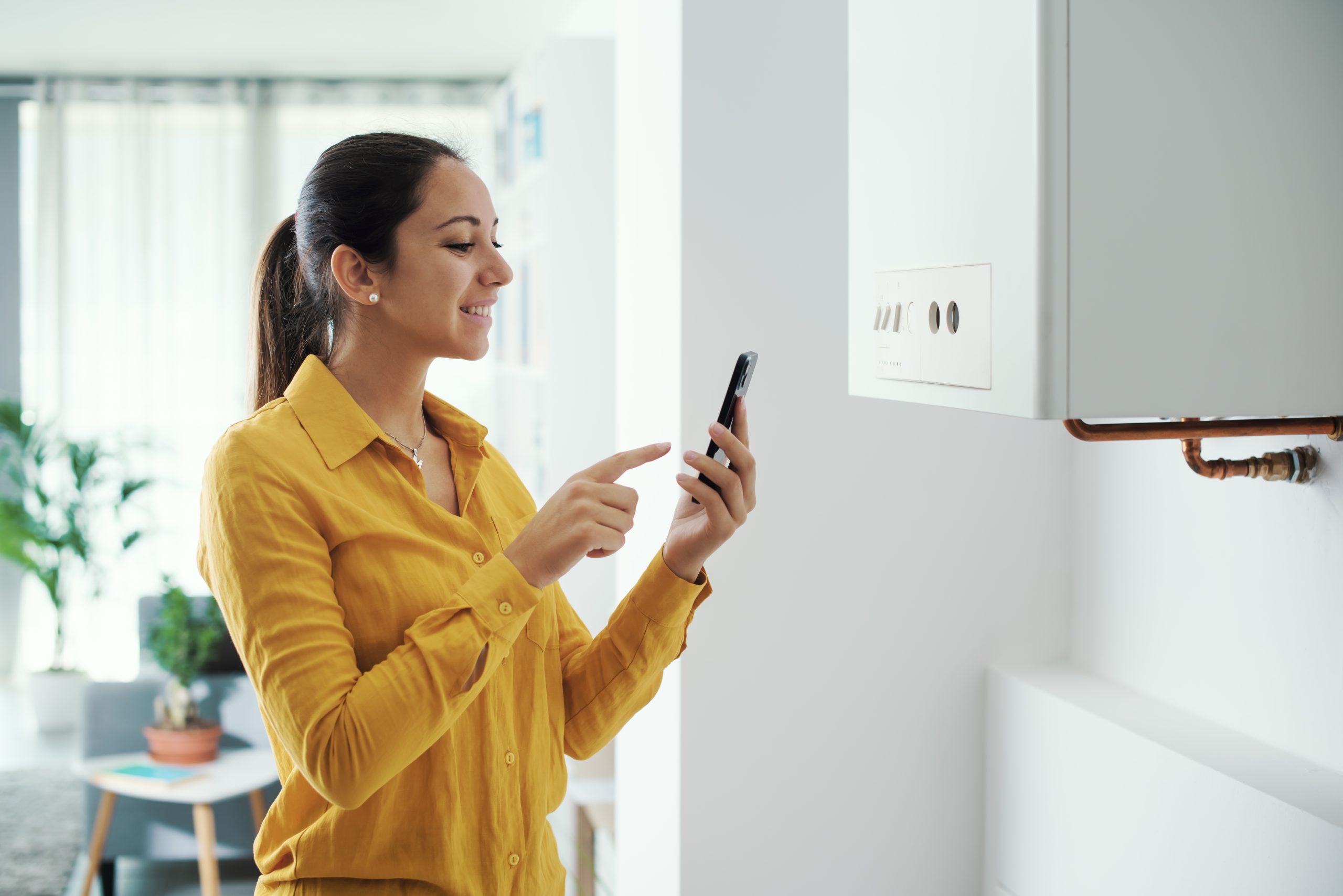Woman in a yellow shirt using her phone to control boiler and smiling
